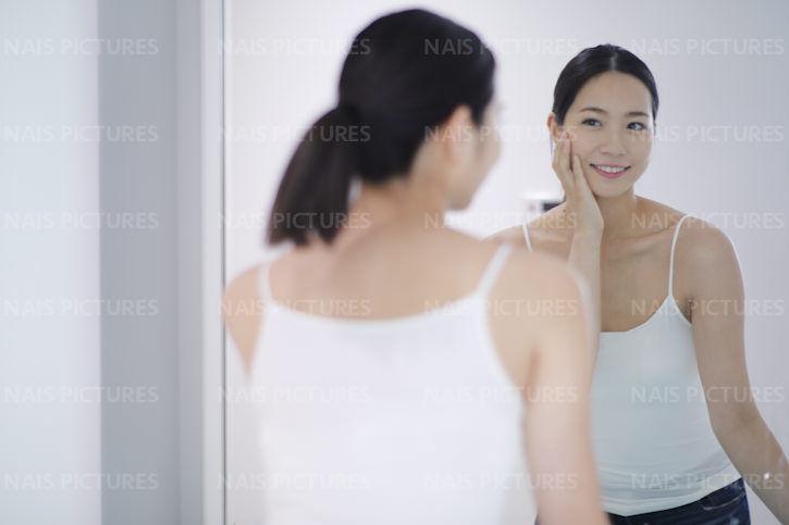 鏡の前でお肌を気にする笑顔の若い女性